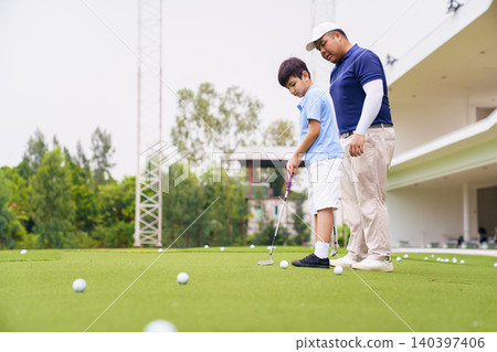Golf instructor teaching young student to putt at practice green Golf instructor teaching young student to putt at practice green 140397406