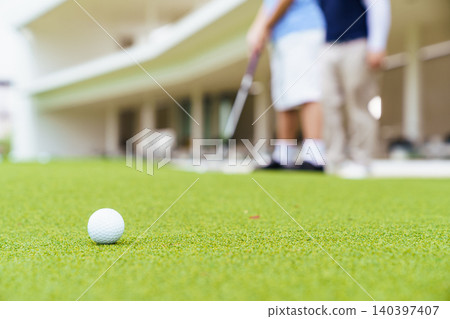 Close up of golf ball on green with blurred instructor and student Close up of golf ball on green with blurred instructor and student 140397407
