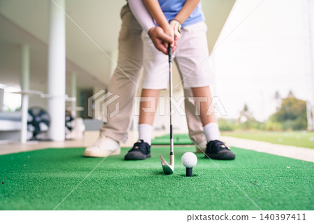 Professional coach guiding student for golf swing on green mat Professional coach guiding student for golf swing on green mat 140397411