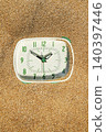 a mint green clock partially buried in sand 140397446