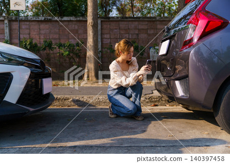 Woman inspecting damaged car bumper after minor accident Woman inspecting damaged car bumper after minor accident 140397458