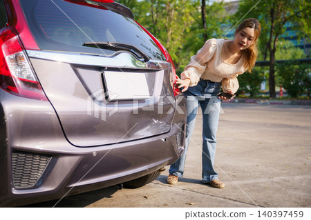 Woman inspecting damaged car bumper after minor accident Woman inspecting damaged car bumper after minor accident 140397459