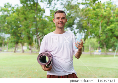 Healthy lifestyle man posing with yoga mat and bottle outdoors 140397481