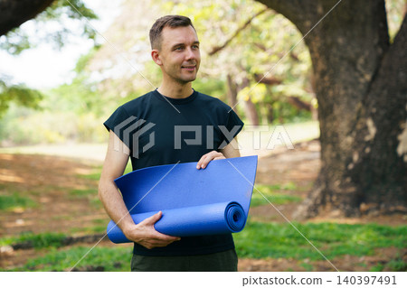 Man holding blue yoga mat in park for outdoor workout Man holding blue yoga mat in park for outdoor workout 140397491