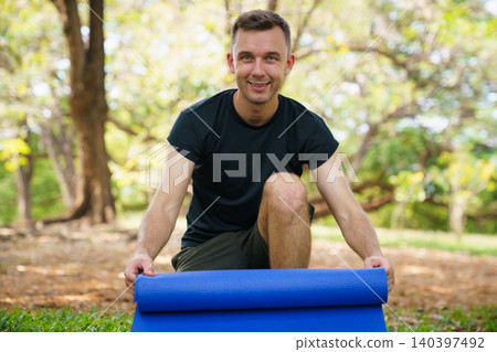 Fit man preparing exercise mat for outdoor yoga in the park Fit man preparing exercise mat for outdoor yoga in the park 140397492