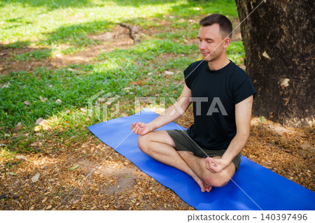 Peaceful young man doing yoga meditation under large tree Peaceful young man doing yoga meditation under large tree 140397496