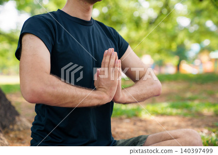 Man practicing meditation in prayer pose on yoga mat in park Man practicing meditation in prayer pose on yoga mat in park 140397499