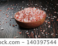 Wooden bowl filled with pink Himalayan salt crystals on dark wooden table, natural mineral seasoning for healthy cooking and spa concepts. 140397544