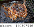 Grilled chicken carcass in metal barbecue basket over hot coals. 140397546