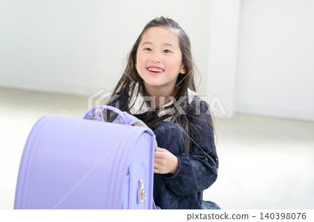 A smiling Japanese girl sitting behind a schoolbag. A smiling Japanese girl sitting behind a schoolbag. 140398076