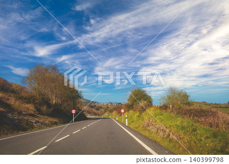 Driving a car on a highway. View from the windscreen of landscape with asphalt road, hills with trees and clear blue sky. Spain, Europe. Driving a car on a highway. View from the windscreen of landscape with asphalt road, hills with trees and clear blue sky. Spain, Europe. 140399798