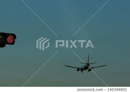 The rear view of a passenger plane flying in the twilight sky and the silhouette of a red traffic light. The rear view of a passenger plane flying in the twilight sky and the silhouette of a red traffic light. 140399802