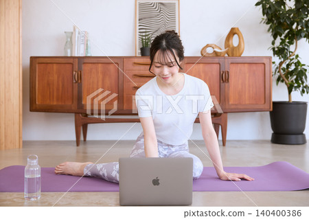 A young woman doing yoga at home while looking at her laptop. 140400386