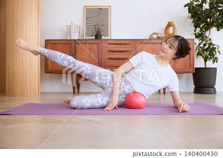 A young woman doing Pilates at home using a balance ball. A young woman doing Pilates at home using a balance ball. 140400430