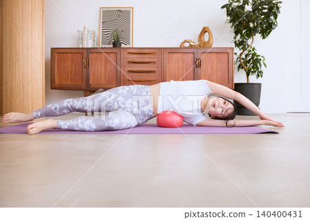 A woman performing a side-bend stretch at home using a ball on a yoga mat. A woman performing a side-bend stretch at home using a ball on a yoga mat. 140400431