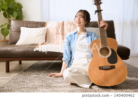A smiling young woman holding an acoustic guitar in her living room. A smiling young woman holding an acoustic guitar in her living room. 140400462