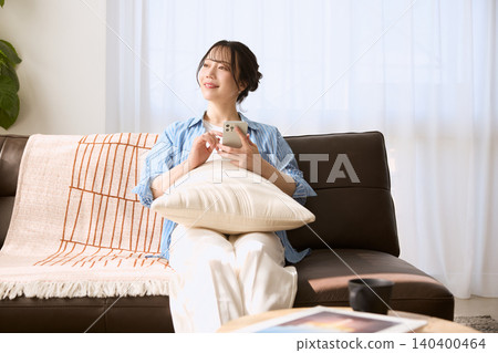 A young woman relaxing on the living room sofa with her smartphone in hand. 140400464