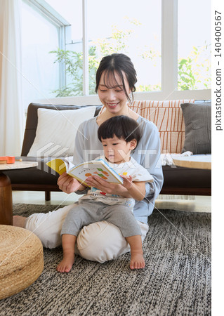 A smiling mother reading a picture book to her child in the living room. A smiling mother reading a picture book to her child in the living room. 140400567