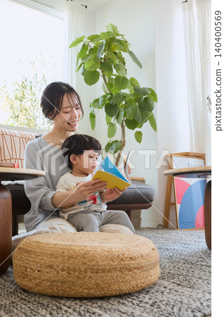一位母親坐在客廳的沙發上,唸圖畫書給孩子聽。 一位母親坐在客廳的沙發上,唸圖畫書給孩子聽。 140400569