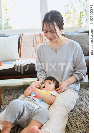 A smiling mother brushes her child's teeth in the living room. A smiling mother brushes her child's teeth in the living room. 140400571