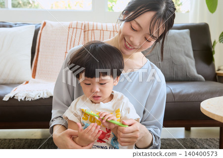 A smiling young mother teaches her child how to brush their teeth in the living room. A smiling young mother teaches her child how to brush their teeth in the living room. 140400573