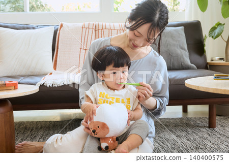 A young mother brushing her child's teeth in the living room. A young mother brushing her child's teeth in the living room. 140400575