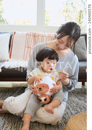 A smiling mother brushes her child's teeth in the living room. A smiling mother brushes her child's teeth in the living room. 140400576