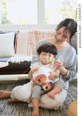 A smiling mother and toddler brushing their child's teeth on the sofa. A smiling mother and toddler brushing their child's teeth on the sofa. 140400577