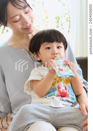 A toddler drinking a pouch beverage on his mother's lap. A toddler drinking a pouch beverage on his mother's lap. 140400600