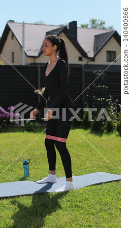 Vertical video. Attractive woman trains her buttocks and leg muscles on a blue carpet outdoors, on the grass in nature. Sports female doing outdoor training. Vertical video. Attractive woman trains her buttocks and leg muscles on a blue carpet outdoors, on the grass in nature. Sports female doing outdoor training. 140400866