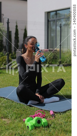 Vertical video. Young sport woman resting, drink water after workout in backyard. Sports female doing outdoor training. Vertical video. Young sport woman resting, drink water after workout in backyard. Sports female doing outdoor training. 140400888
