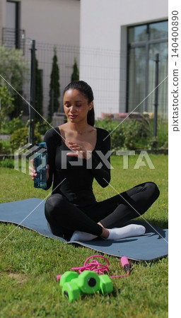 Vertical video. Young sport woman resting, drink water after workout in backyard. Sports female doing outdoor training. Vertical video. Young sport woman resting, drink water after workout in backyard. Sports female doing outdoor training. 140400890