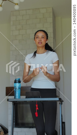 Vertical Video. Beautiful athletic sports woman running on a treadmill at home. Energetic workout athlete training while listening podcast or music in headphones. Vertical Video. Beautiful athletic sports woman running on a treadmill at home. Energetic workout athlete training while listening podcast or music in headphones. 140400895