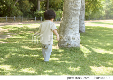 The back view of a toddler walking on the grass in a park in summer. The back view of a toddler walking on the grass in a park in summer. 140400902