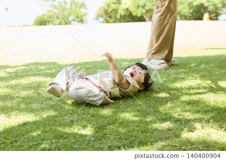 一個哭泣的幼兒躺在草地上,父母在一旁照顧。 一個哭泣的幼兒躺在草地上,父母在一旁照顧。 140400904