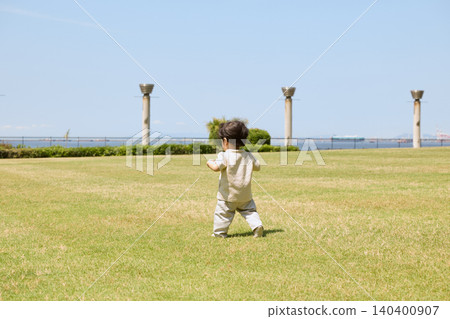 The back view of a toddler toddling across a grassy park. The back view of a toddler toddling across a grassy park. 140400907