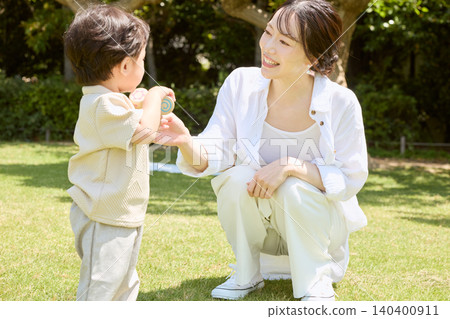 A young mother smiles as she plays with her small child on the park's lawn. A young mother smiles as she plays with her small child on the park's lawn. 140400911