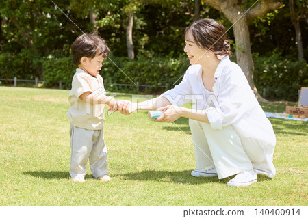 A young boy playing on the park's lawn, holding his mother's hand. 140400914