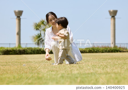 一位母親和她的小兒子在草地公園吹肥皂泡。 140400925
