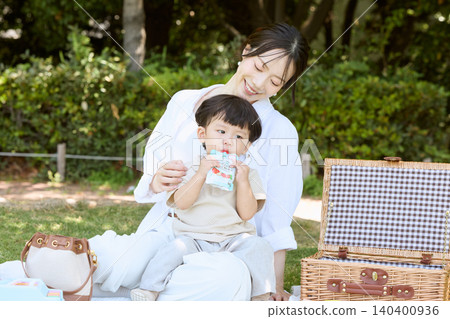 A mother and toddler enjoying a picnic in the park, drinking a jelly drink. A mother and toddler enjoying a picnic in the park, drinking a jelly drink. 140400936