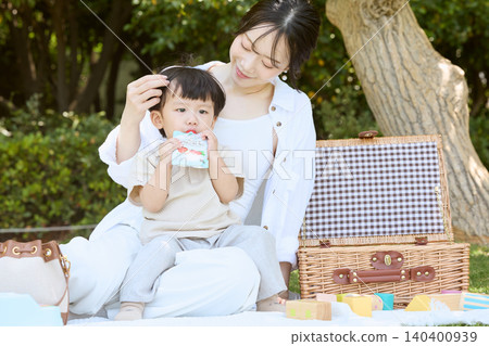 一位母親和孩子在公園裡野餐,孩子正在吃嬰兒食品。 一位母親和孩子在公園裡野餐,孩子正在吃嬰兒食品。 140400939