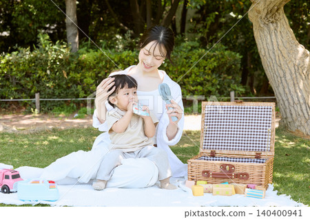 一位母親帶著年幼的兒子在公園野餐,在夏天用便攜式風扇降溫。 一位母親帶著年幼的兒子在公園野餐,在夏天用便攜式風扇降溫。 140400941