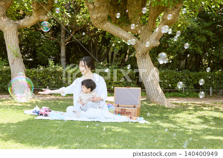 A mother and baby enjoying a picnic in the park, blowing soap bubbles. A mother and baby enjoying a picnic in the park, blowing soap bubbles. 140400949