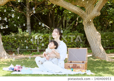 一位母親帶著嬰兒在公園野餐,抬頭看著肥皂泡。 一位母親帶著嬰兒在公園野餐,抬頭看著肥皂泡。 140400953