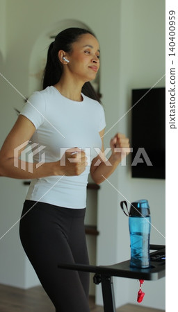 Vertical Video. Athletic woman running on treadmill during home cardio workout in apartment interior. Fitness challenge and burning calories. Vertical Video. Athletic woman running on treadmill during home cardio workout in apartment interior. Fitness challenge and burning calories. 140400959