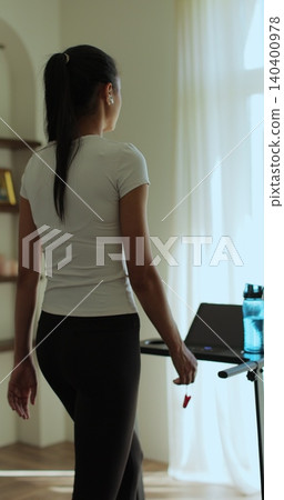 Vertical video. Back view Female is doing cardio workout training on treadmill at home. Running on treadmill. Home fitness activity. Vertical video. Back view Female is doing cardio workout training on treadmill at home. Running on treadmill. Home fitness activity. 140400978
