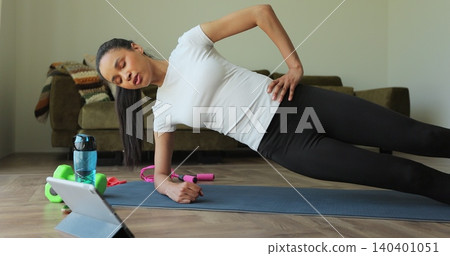 Young woman doing sports while watching training video on tablet at home. Sport, fitness, health and lifestyle concept. Watching online fitness training lessons. Young woman doing sports while watching training video on tablet at home. Sport, fitness, health and lifestyle concept. Watching online fitness training lessons. 140401051