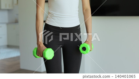 Close up young sports girl in leggings does exercises with dumbbells. Healthy lifestyle. Woman goes in for sports outdoor at home. Close up young sports girl in leggings does exercises with dumbbells. Healthy lifestyle. Woman goes in for sports outdoor at home. 140401065