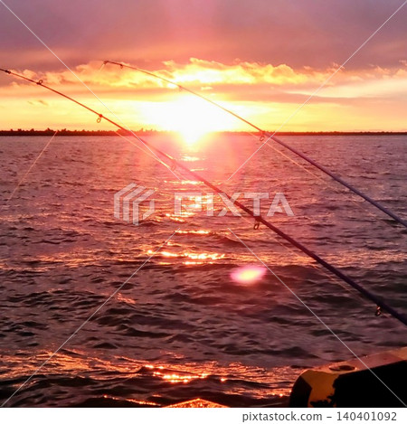 A beautiful sunset sinking below the horizon, a fishing rod, and the sea surface bathed in golden light during the magic hour (dusk scene). A beautiful sunset sinking below the horizon, a fishing rod, and the sea surface bathed in golden light during the magic hour (dusk scene). 140401092