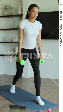 Vertical video. Athletic young woman in sportswear training at home, performing squats with dumbbells in her hands, enjoying a healthy lifestyle. Athletic woman doing training. Vertical video. Athletic young woman in sportswear training at home, performing squats with dumbbells in her hands, enjoying a healthy lifestyle. Athletic woman doing training. 140401101